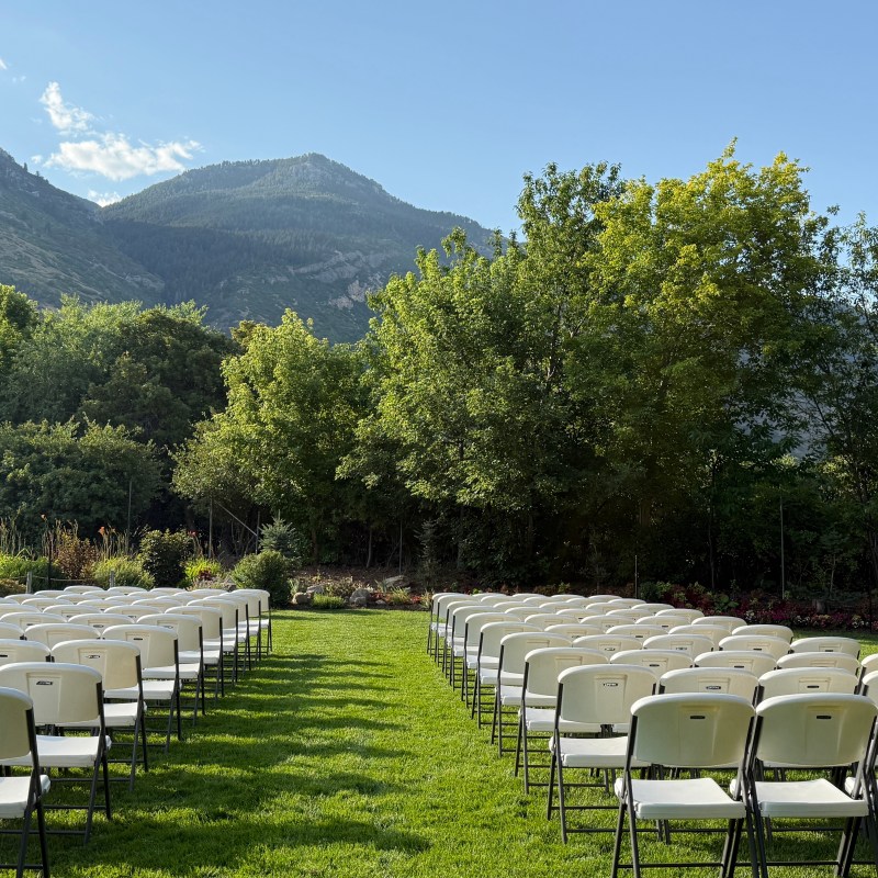 Outdoor ceremony setup with rows of white chairs facing mountains and trees.