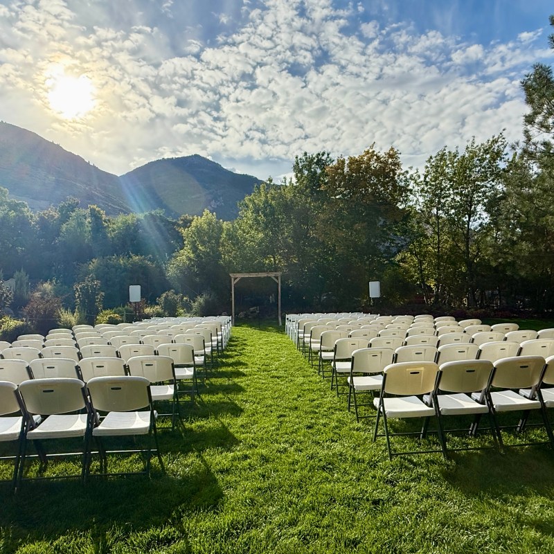 Outdoor wedding setup with rows of white chairs facing an arch and a sunny sky.
