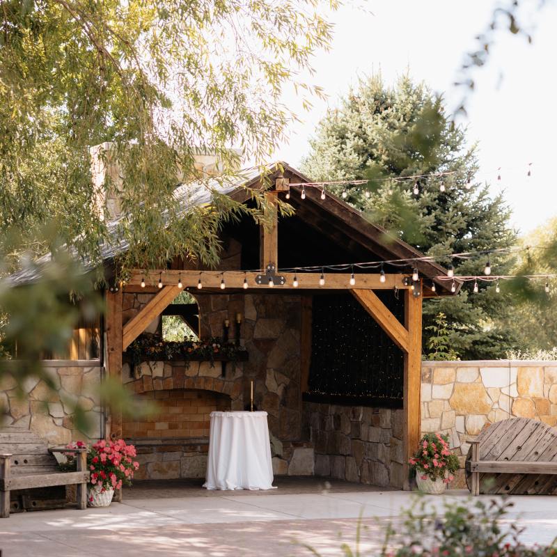 Outdoor patio with wooden structure, string lights, stone fireplace, and flower pots.