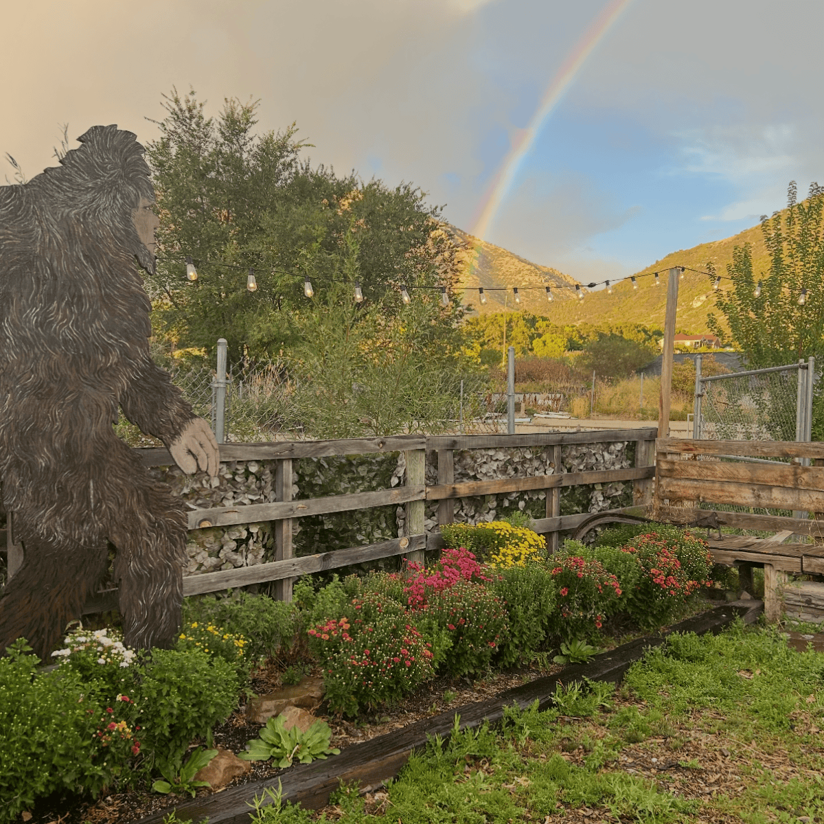 Garden with Bigfoot cutout, flowers, and a rainbow in the sky.